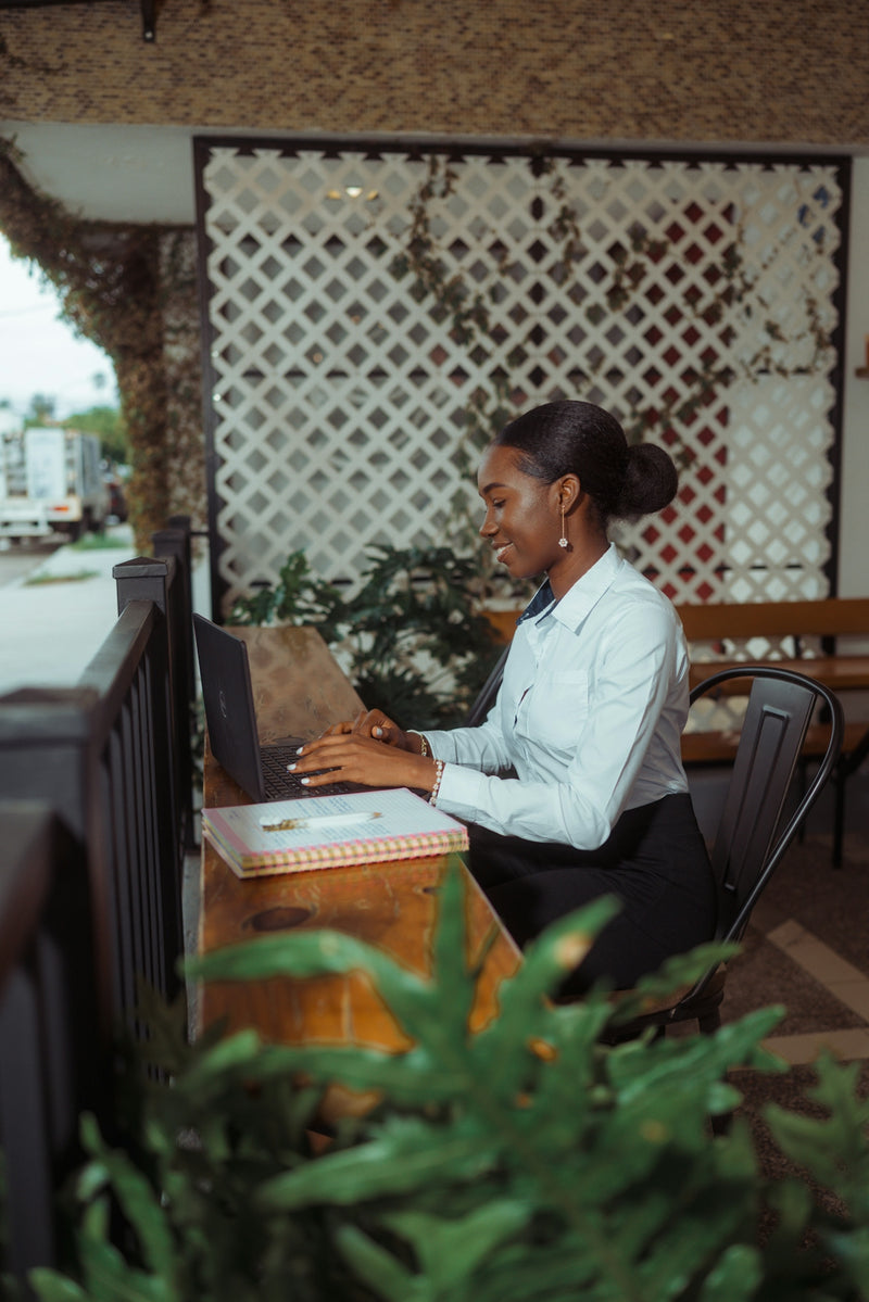 A woman smiling while working on a laptop outdoors