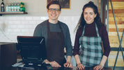 Two smiling cafe workers stand behind a counter