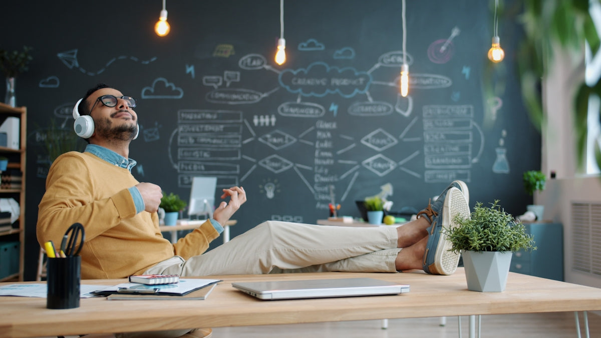 Man wearing headphones plays air guitar at desk
