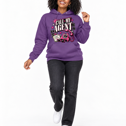 A woman modeling a purple pullover hoodie with a colorful graphic print that reads 'CALL ME AGENT' on the front, paired with dark gray jeans and white sneakers, against a plain white background.