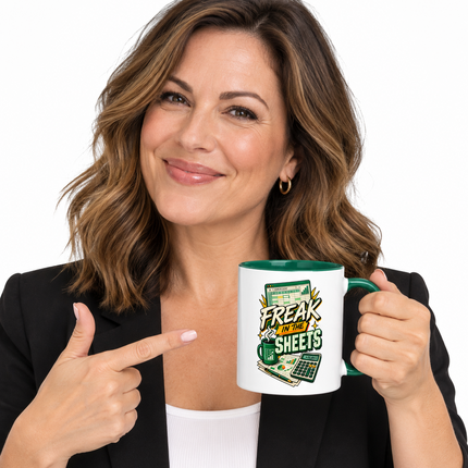 A woman in a black blazer and white top holds a white ceramic mug with a green handle and interior. The mug features a green and yellow graphic with the text 'FREAKY SHEETS' and a calculator illustration.