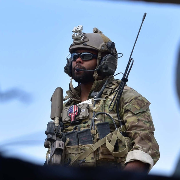 Person in military gear with a helmet and sunglasses, standing outdoors.