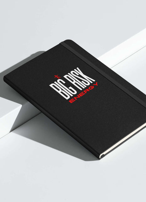 Big Risk Energy Notebook on a white surface, featuring a bold black cover and red lettering for visionary ideas.